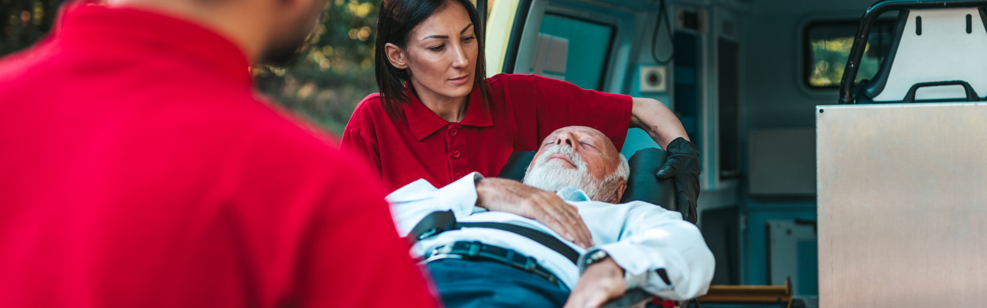 two people carrying elderly man laying in a stretcher inside a vehicle